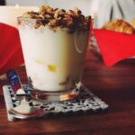 Yogurt servito in una ciotola, con frutta fresca e cereali, su un tavolo.